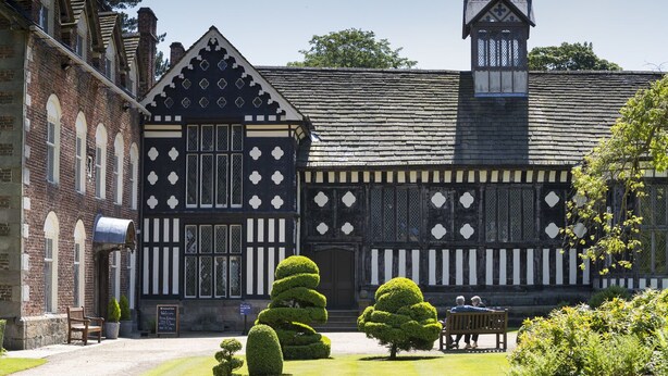 Un edificio de estilo Tudor tradicional, con techo a dos aguas pronunciado, una torre destacada y fachada simétrica con entramado de madera en blanco y negro.
