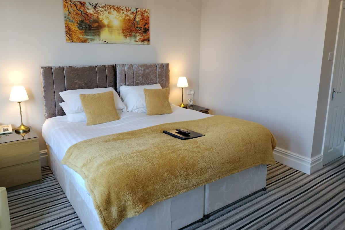 Quarto de hotel com uma cama grande, duas luminárias de cabeceira, mesa de cabeceira com telefone e um quadro na parede.