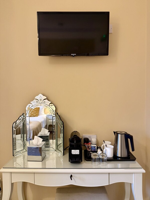 A hotel room with a TV mounted on the wall, a bedside table with a tissue box, a coffee maker, and a glass of water.