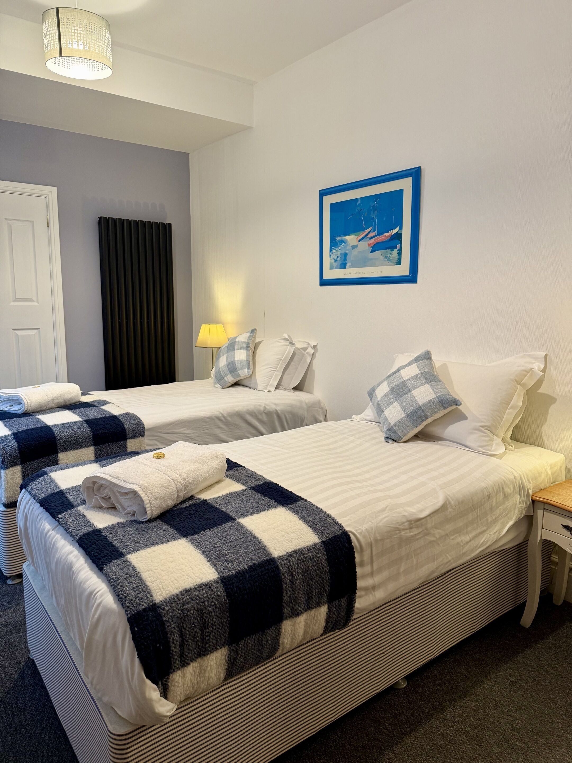 Une chambre d’hôtel avec deux lits, un tableau au mur, une lampe et une porte.