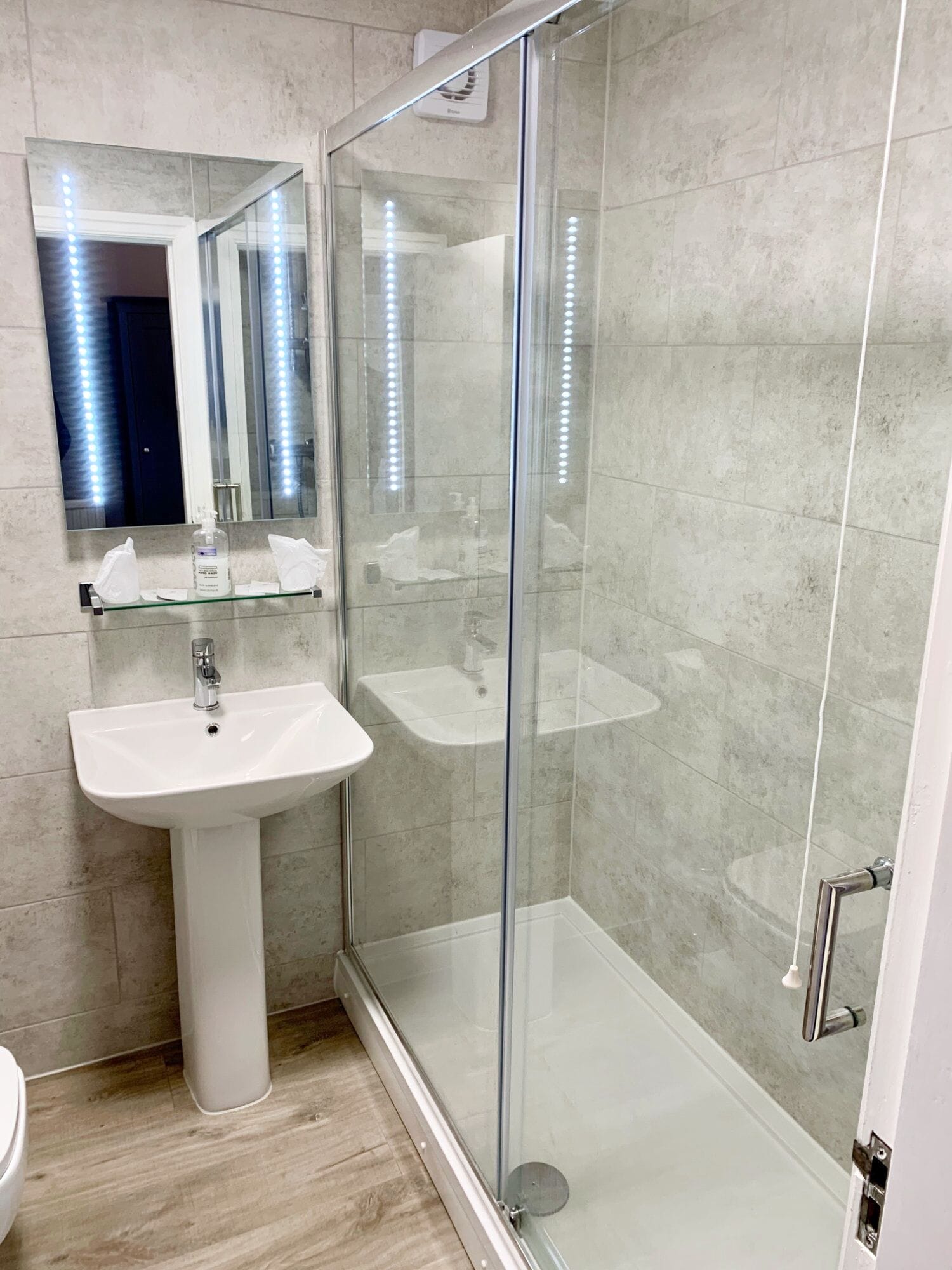 A modern bathroom with a glass-enclosed shower, a pedestal sink, and a mirror with LED lights.
