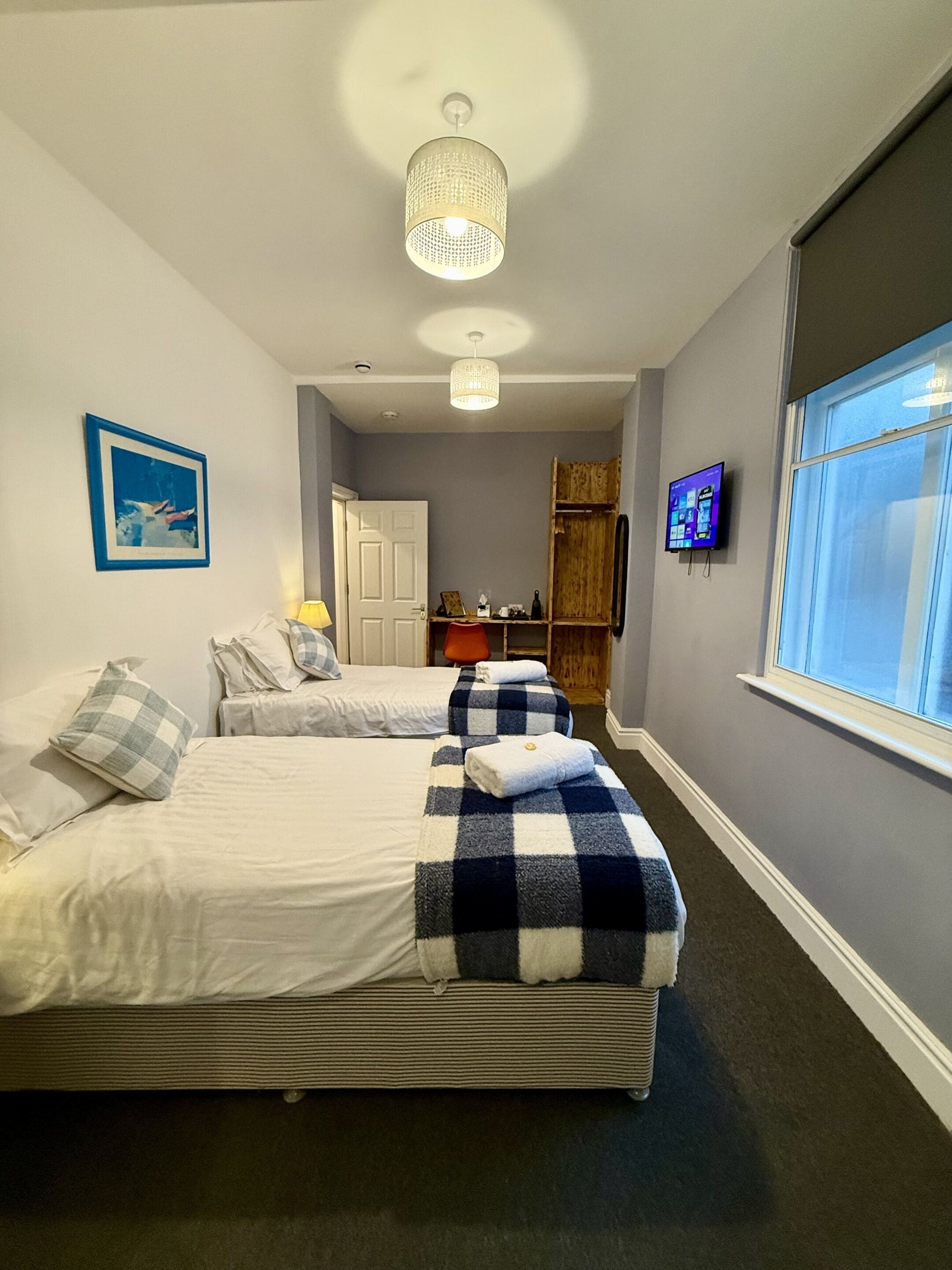A hotel room with two beds, a television, a window, and a ceiling light fixture.