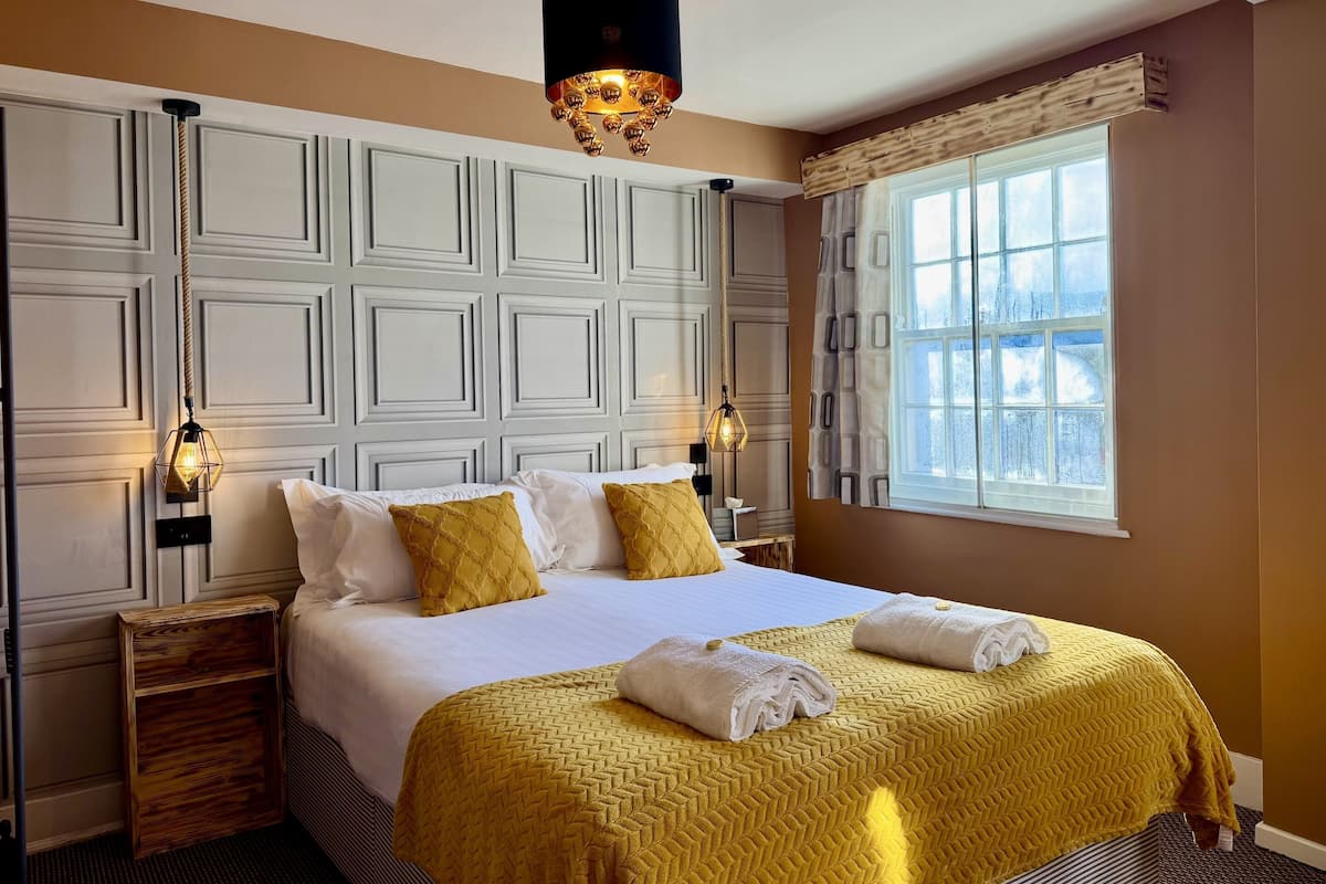 Habitación de hotel con una cama grande, dos mesitas de noche, una ventana con cortinas y una lámpara decorativa en el techo.