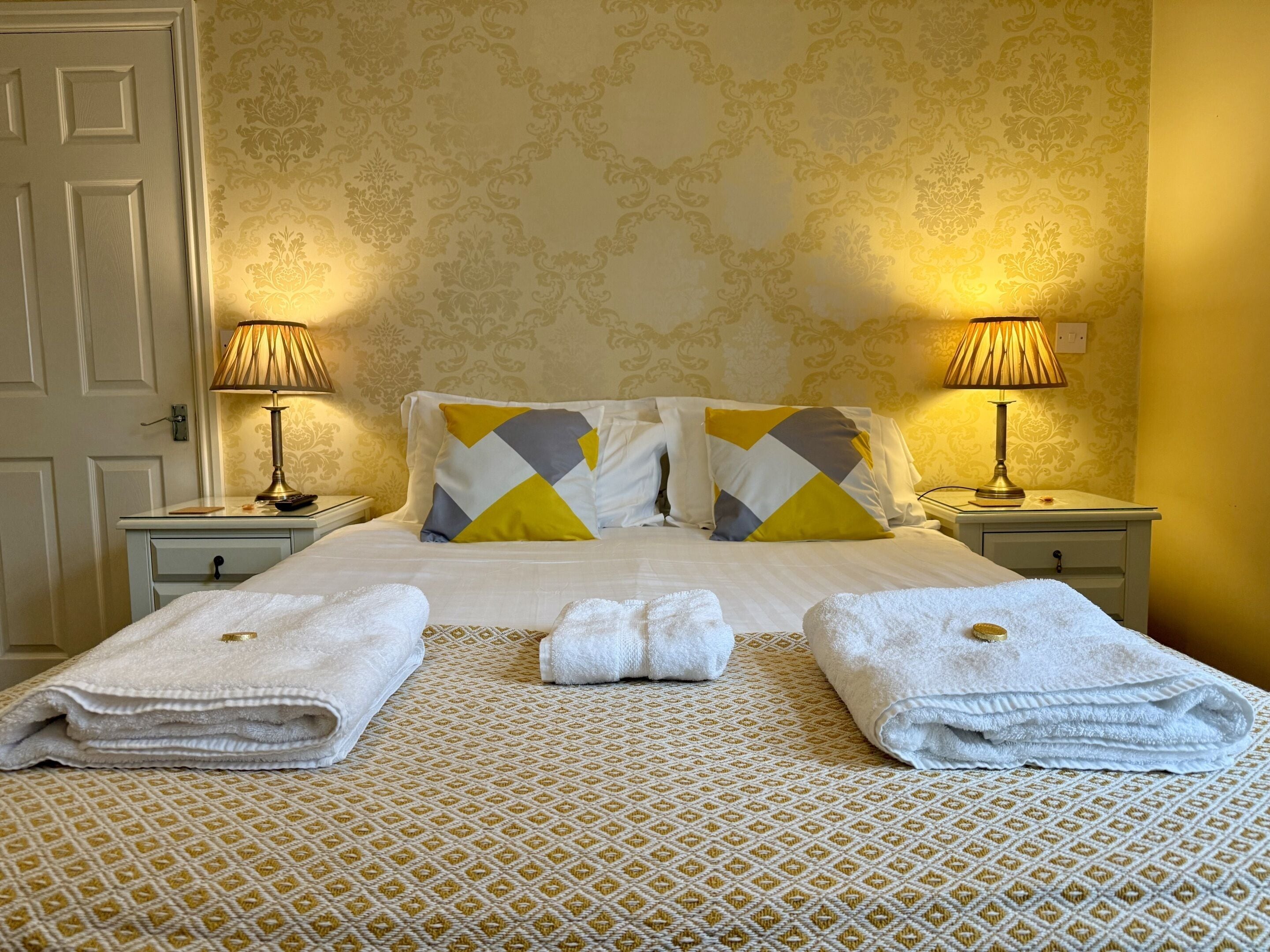 A neatly made bed with two pillows, two bedside lamps, and two towels on the bed.