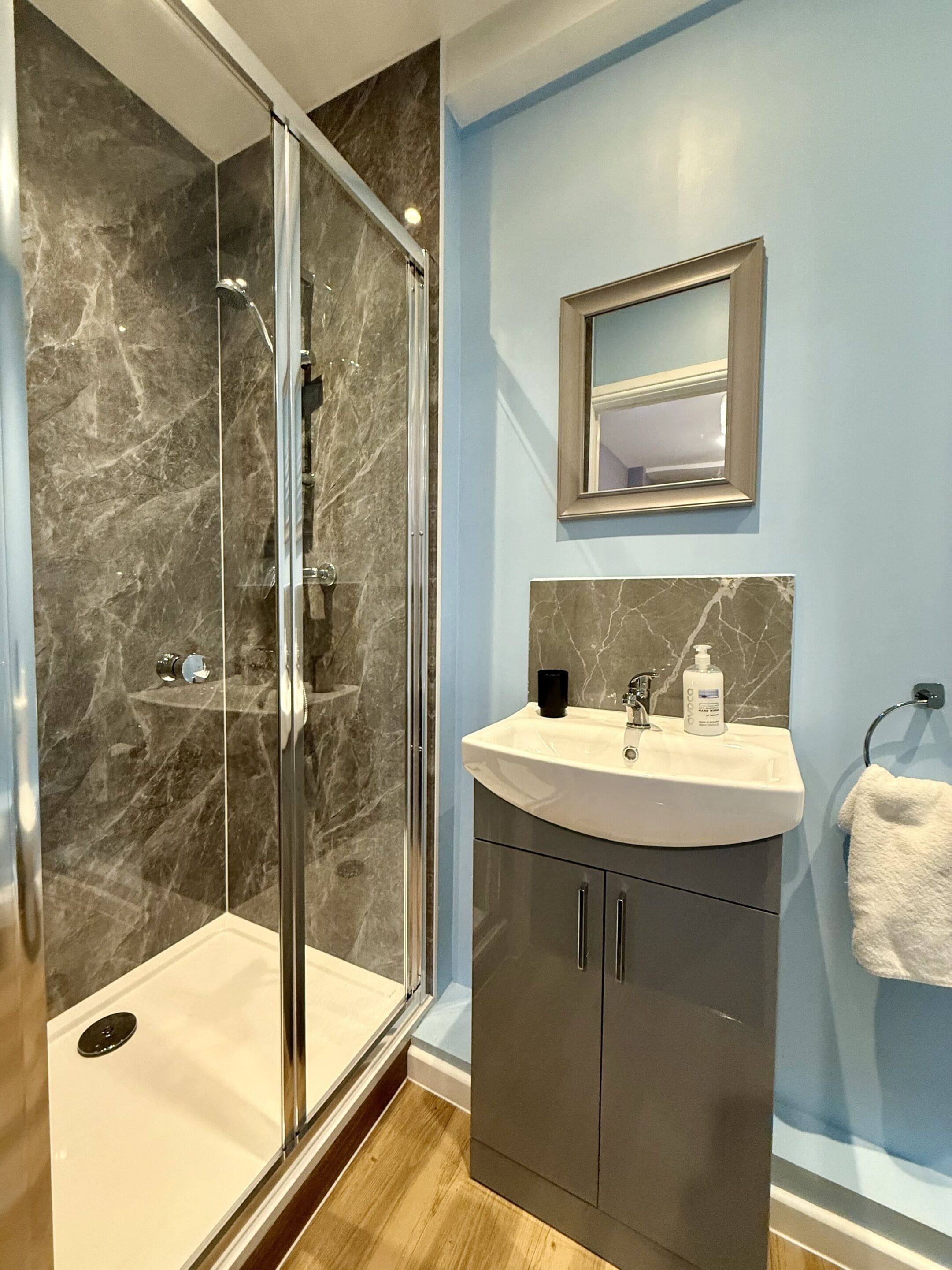 A modern bathroom with a glass-enclosed shower, a sink with a marble countertop, and a mirror above the sink.