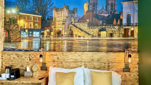 A hotel room with a bed, bedside tables, and a view of a historic cityscape with a river. - The Crescent Guest House (York)