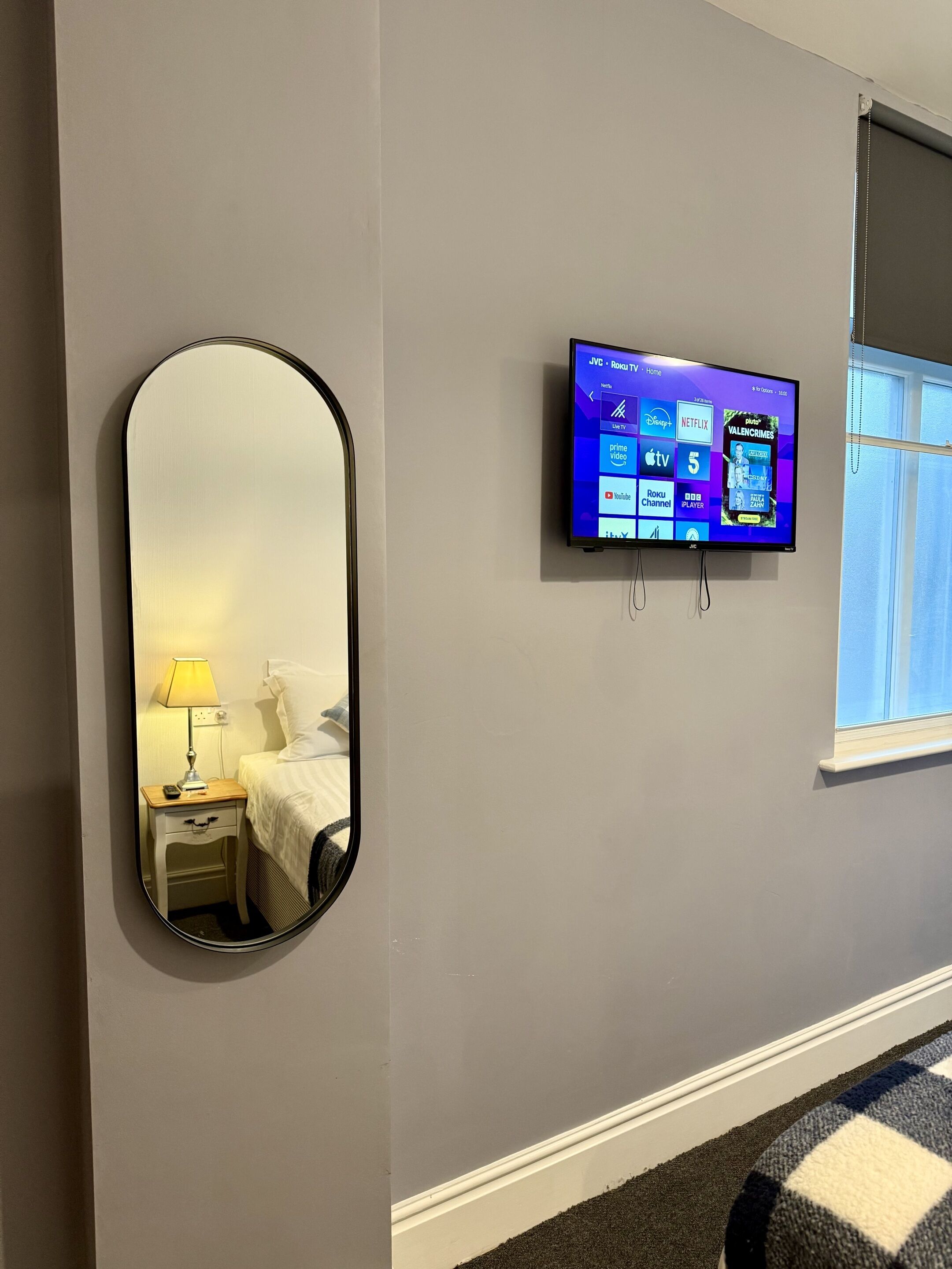 Une chambre d’hôtel dotée d’un grand miroir, d’un téléviseur à écran plat fixé au mur et d’une fenêtre avec des rideaux.