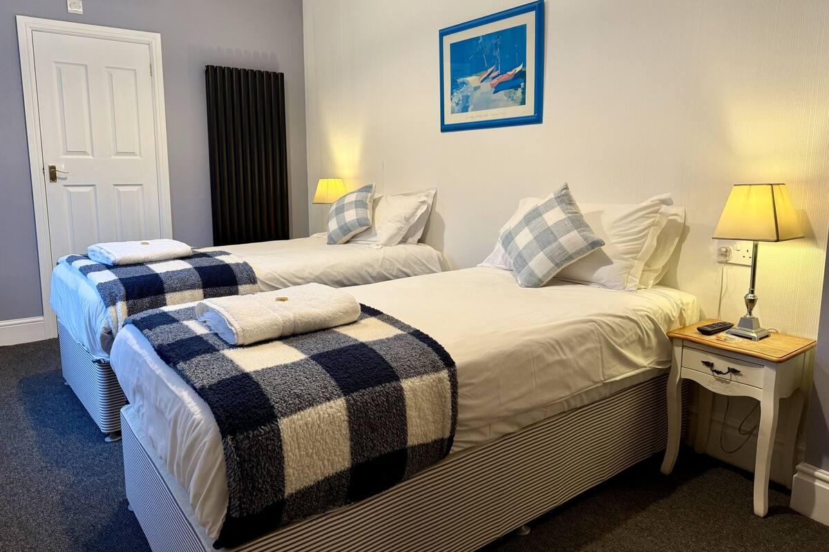 Una habitación de hotel con dos camas, una mesita de noche, una lámpara y un cuadro en la pared.