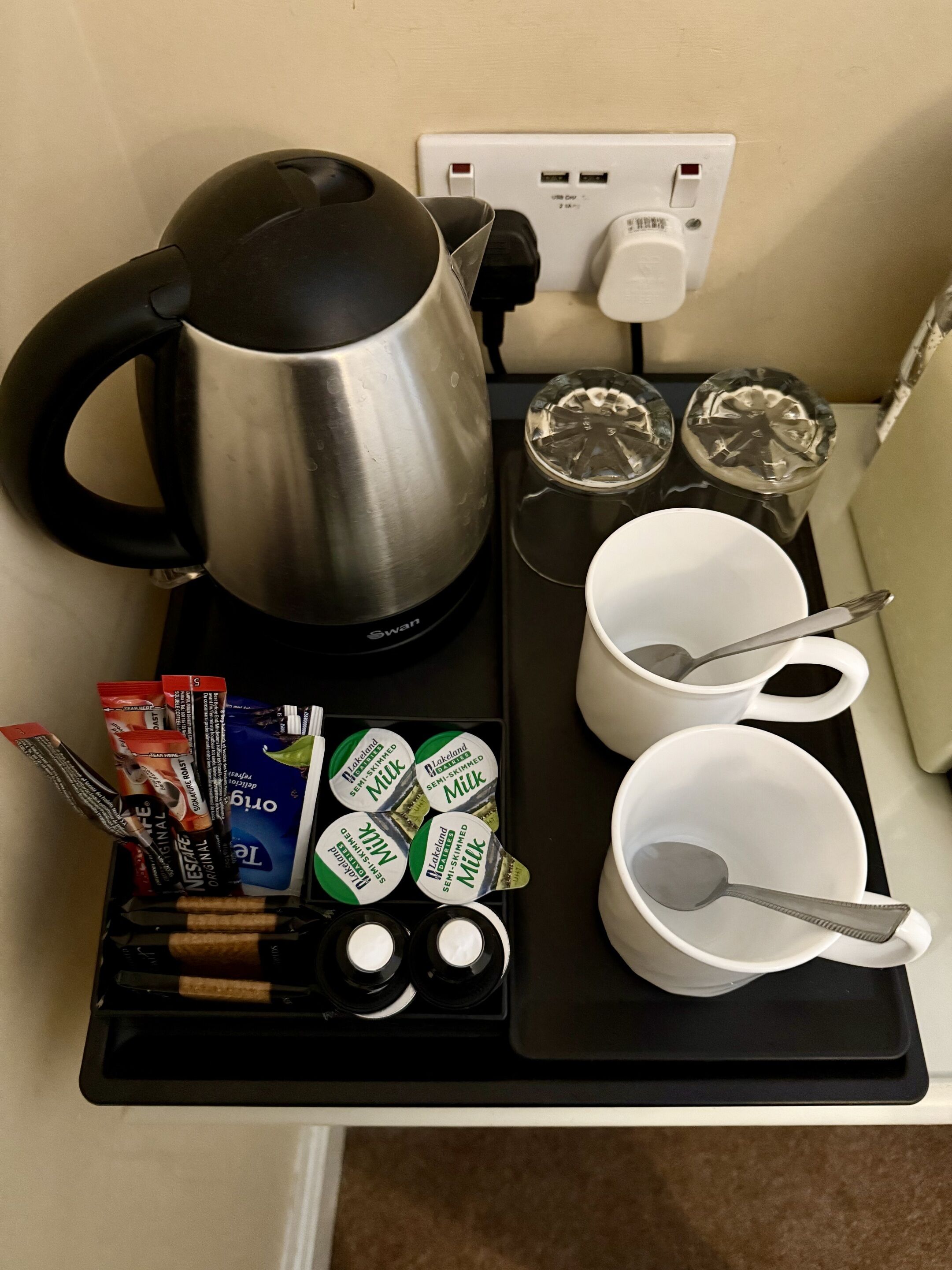 A kitchen counter with a kettle, cups, a tray with food items, and a power outlet.