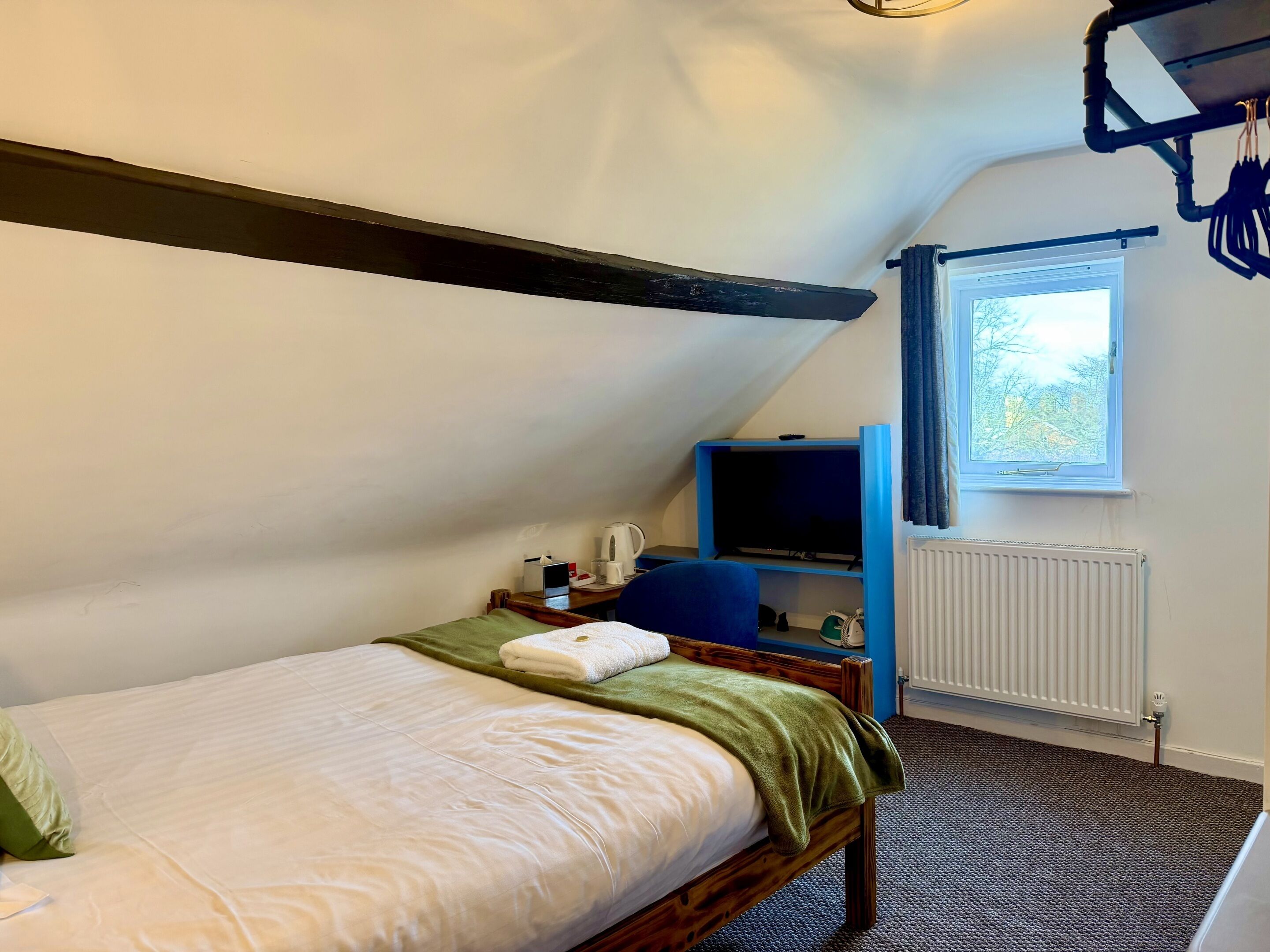 Un dormitorio pequeño y acogedor con una cama individual, un escritorio con silla, un televisor y una ventana con cortinas.