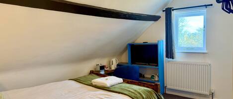 Un dormitorio pequeño y acogedor con una cama individual, un escritorio con silla, un televisor y una ventana con cortinas.