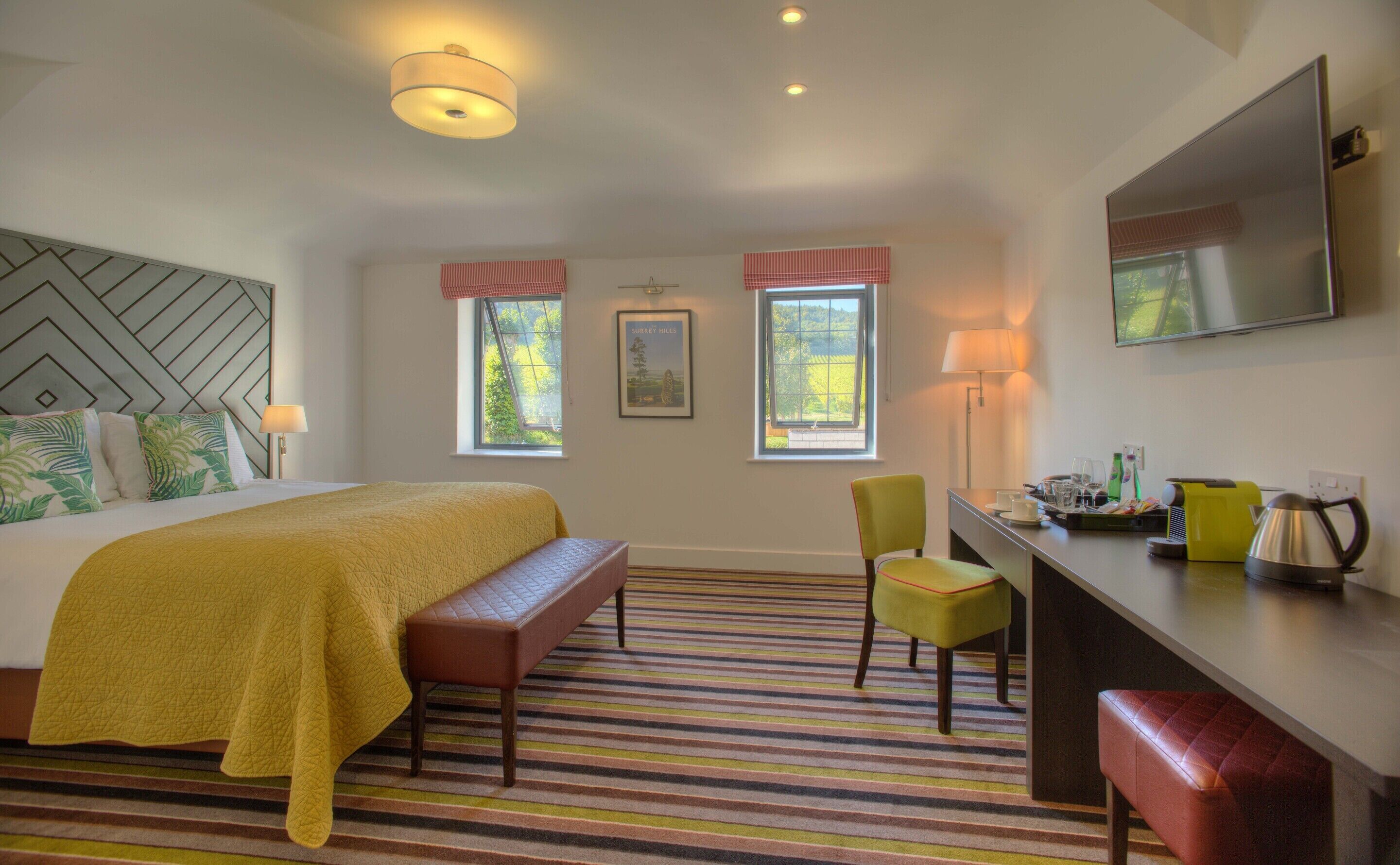 A hotel room with a bed, bench, desk, chair, and a TV on the wall.