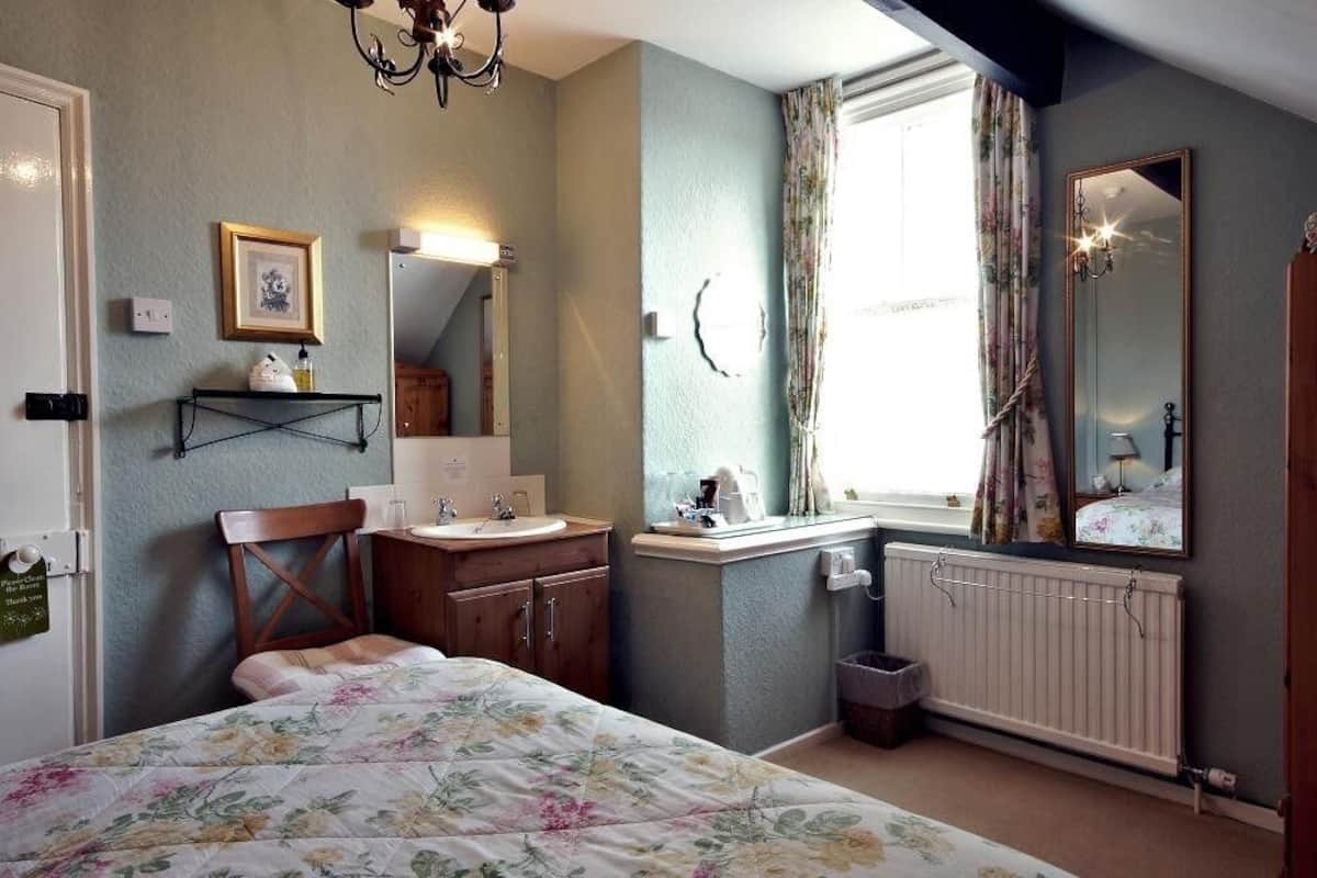 A bedroom with a bed, a bedside table, a mirror, a window with curtains, and a radiator.
