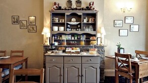 A dining area with a wooden table and chairs, a buffet counter with various food items, and wall-mounted artwork. - The Farthings Guest House (York)