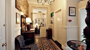 A hallway with patterned carpet, a chandelier, framed artwork, and a door with a sign. - The Farthings Guest House (York)