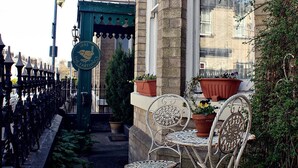 A narrow alley with a row of metal chairs and tables, a green sign with a bird logo, and potted plants on a building's windowsill. - The Farthings Guest House (York)