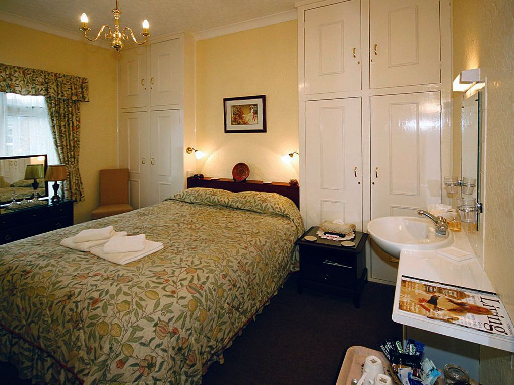 Ein Hotelzimmer mit einem Bett, einem Nachttisch, einer Kommode, einem Spiegel und einem Badezimmer mit Waschbecken und Toilettenartikeln.