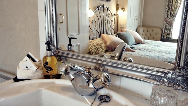 A bathroom with a large mirror, a sink, and a bottle of perfume. - The Farthings Guest House (York)