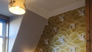 A bedroom with a sloped ceiling, a bed with blue and white bedding, two bedside lamps, and a wall with a bird pattern. - Fraoch House (Edinburgh)