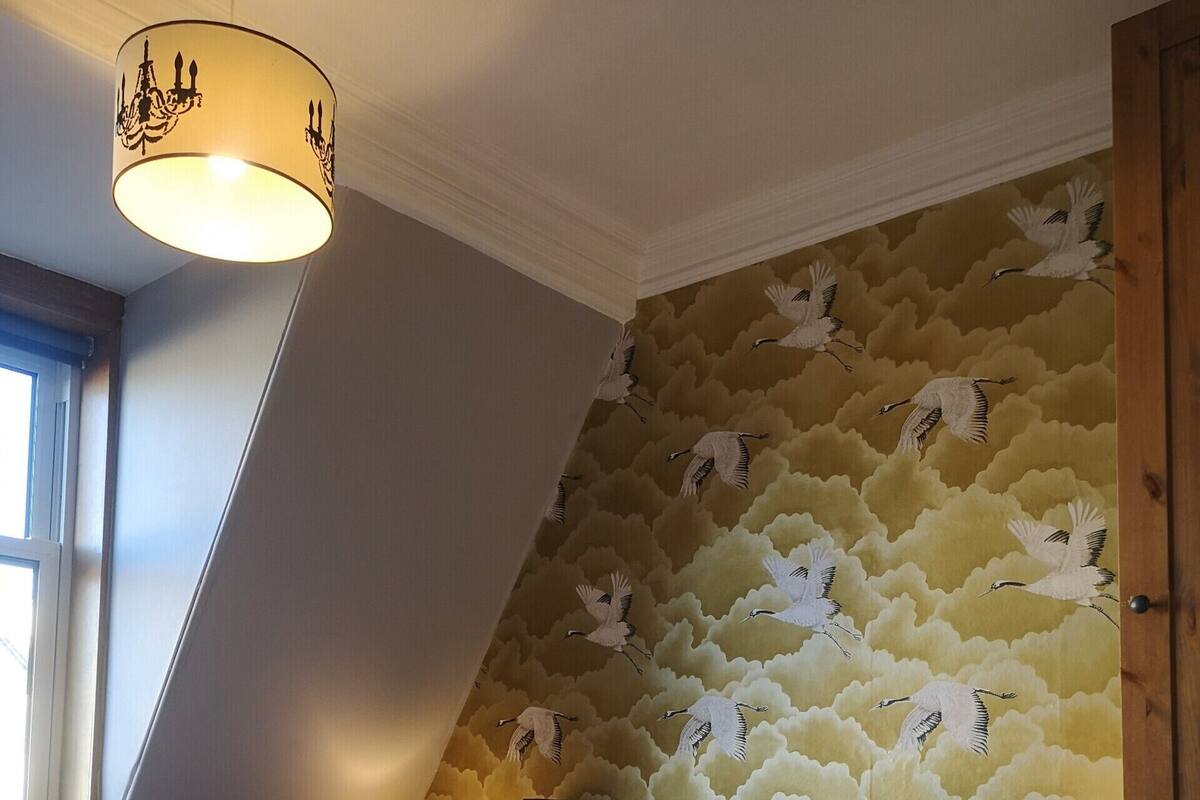 Une chambre avec un plafond en pente, un lit avec une literie bleue et blanche, deux lampes de chevet et un mur orné d’un motif d’oiseaux.