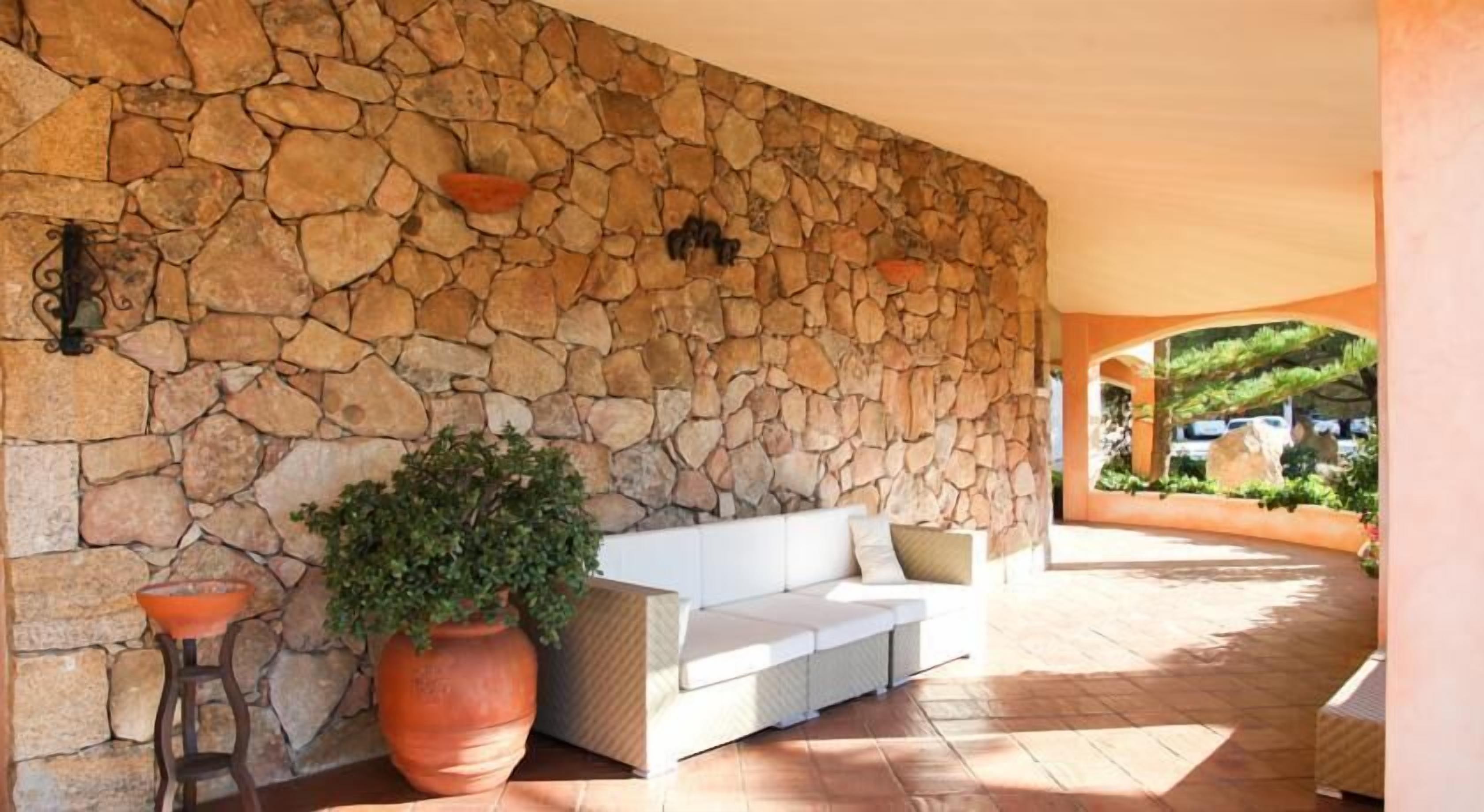 A stone wall, a white sofa, and a large potted plant in a covered outdoor area.