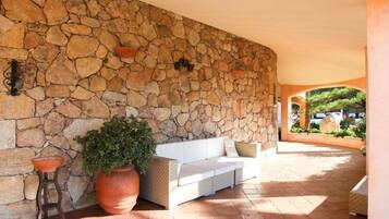 A stone wall, a white sofa, and a large potted plant in a covered outdoor area.