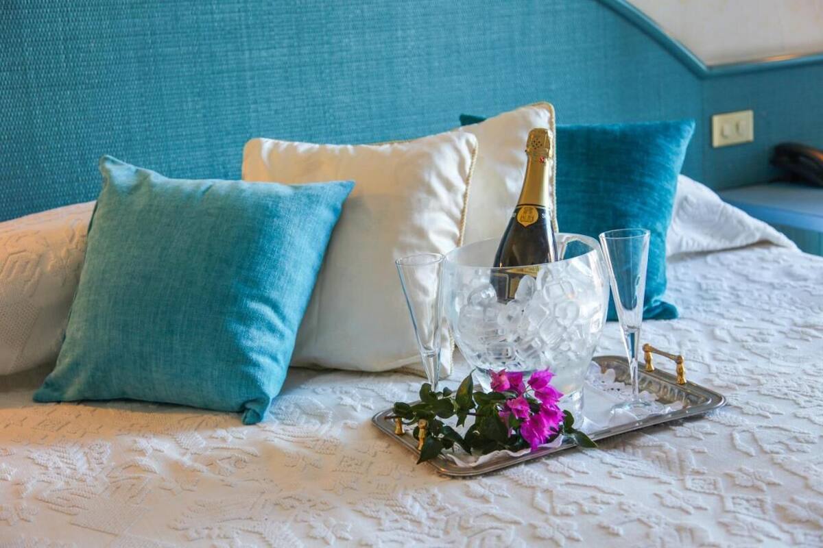 A bed with a white textured bedspread, a bottle of champagne, two glasses, and a tray with a flower.