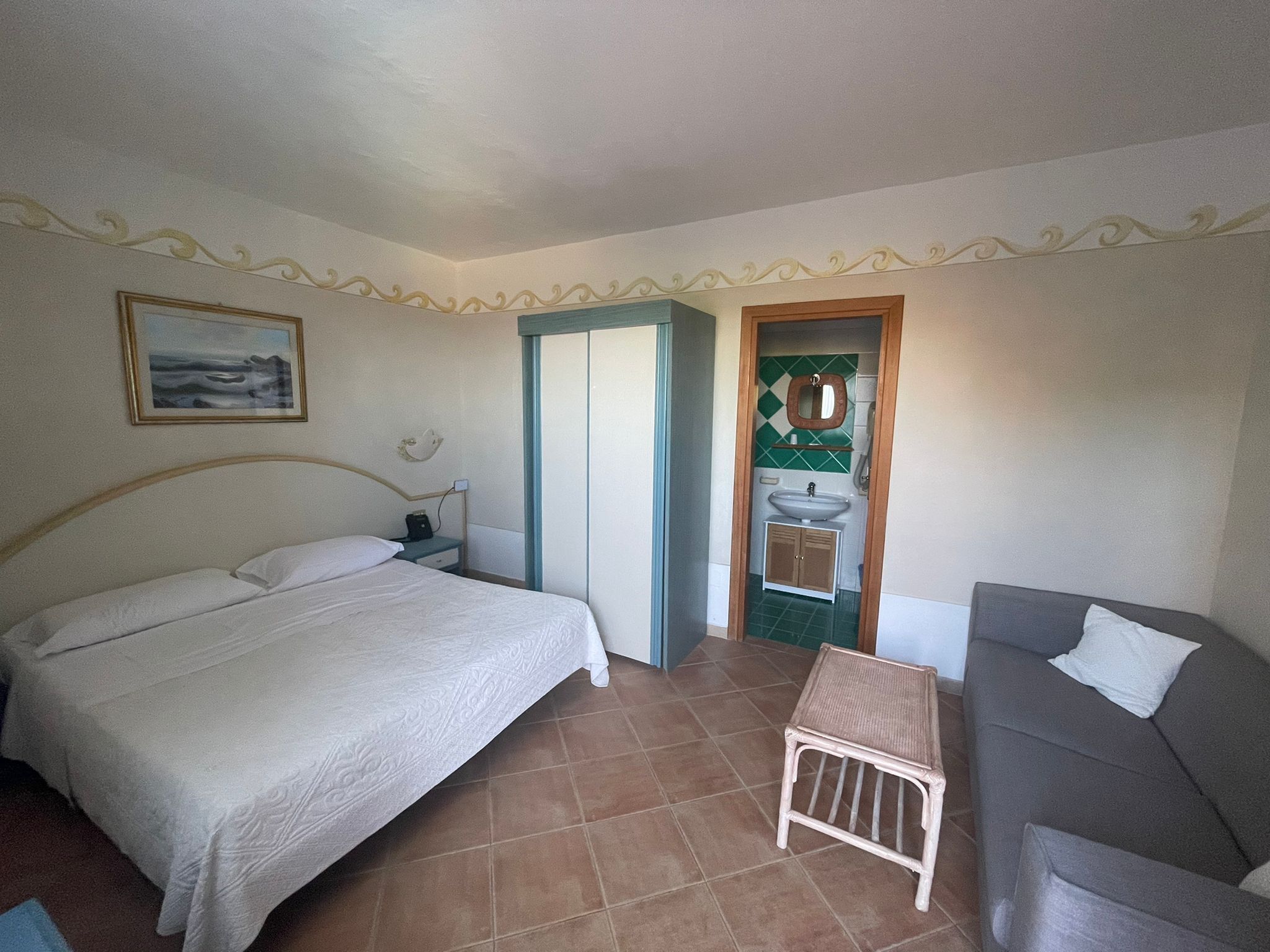 Une chambre à coucher comprenant un lit, une table de chevet, une petite table, un canapé et une salle de bain avec un lavabo et un miroir.
