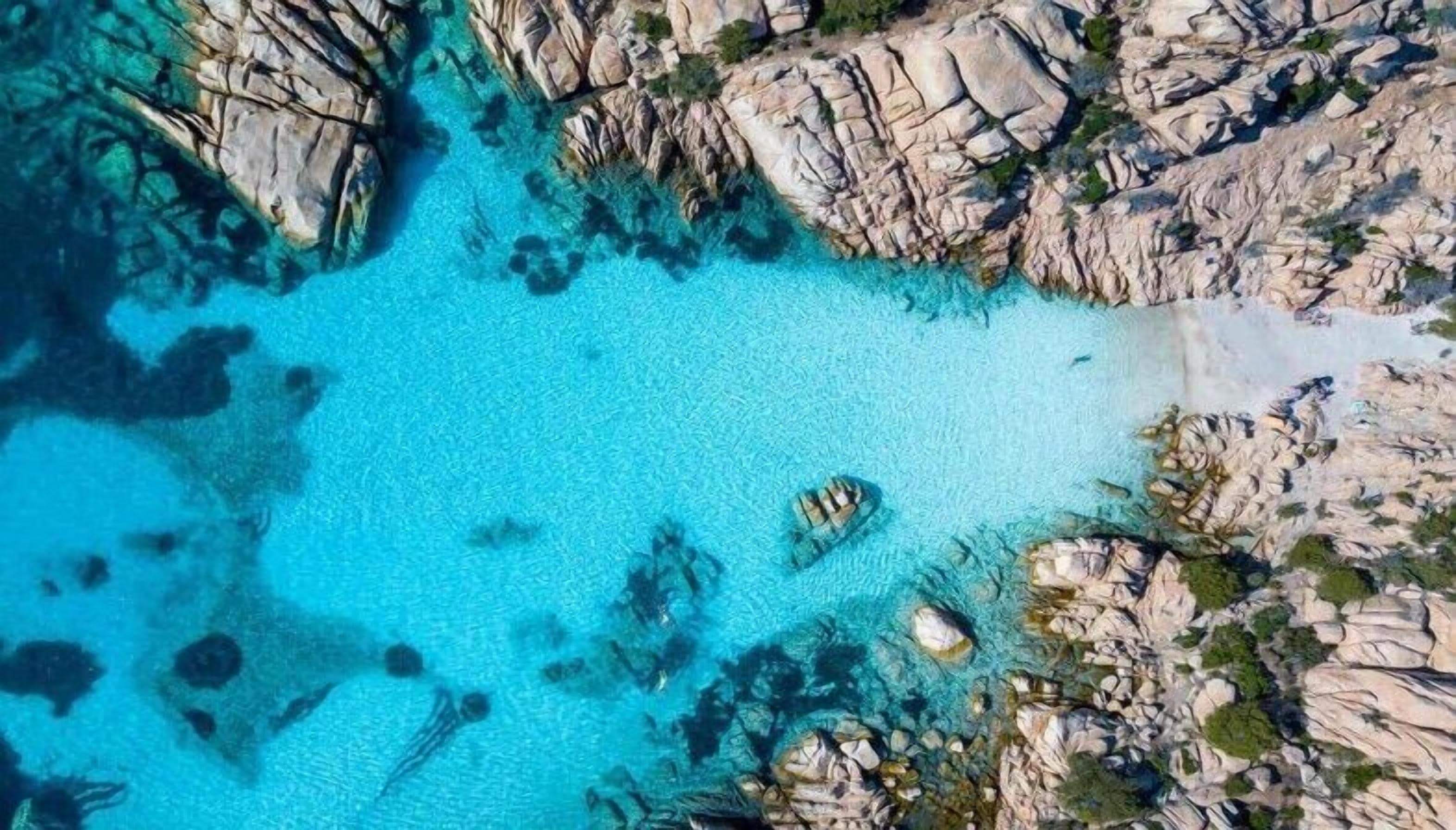 Ein Luftbild einer Küstenregion mit klarem türkisblauem Wasser, Felsformationen und vereinzelter Vegetation.
