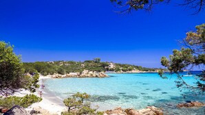 A coastal landscape with clear turquoise waters, rocky shorelines, and a path leading to a sandy beach. - Hotel Micalosu (Arzachena)