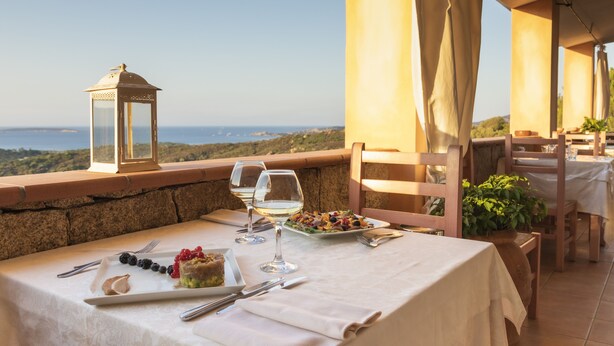 A table set for a meal with a view of the sea, a lantern, and a potted plant. - Hotel Micalosu (Arzachena)