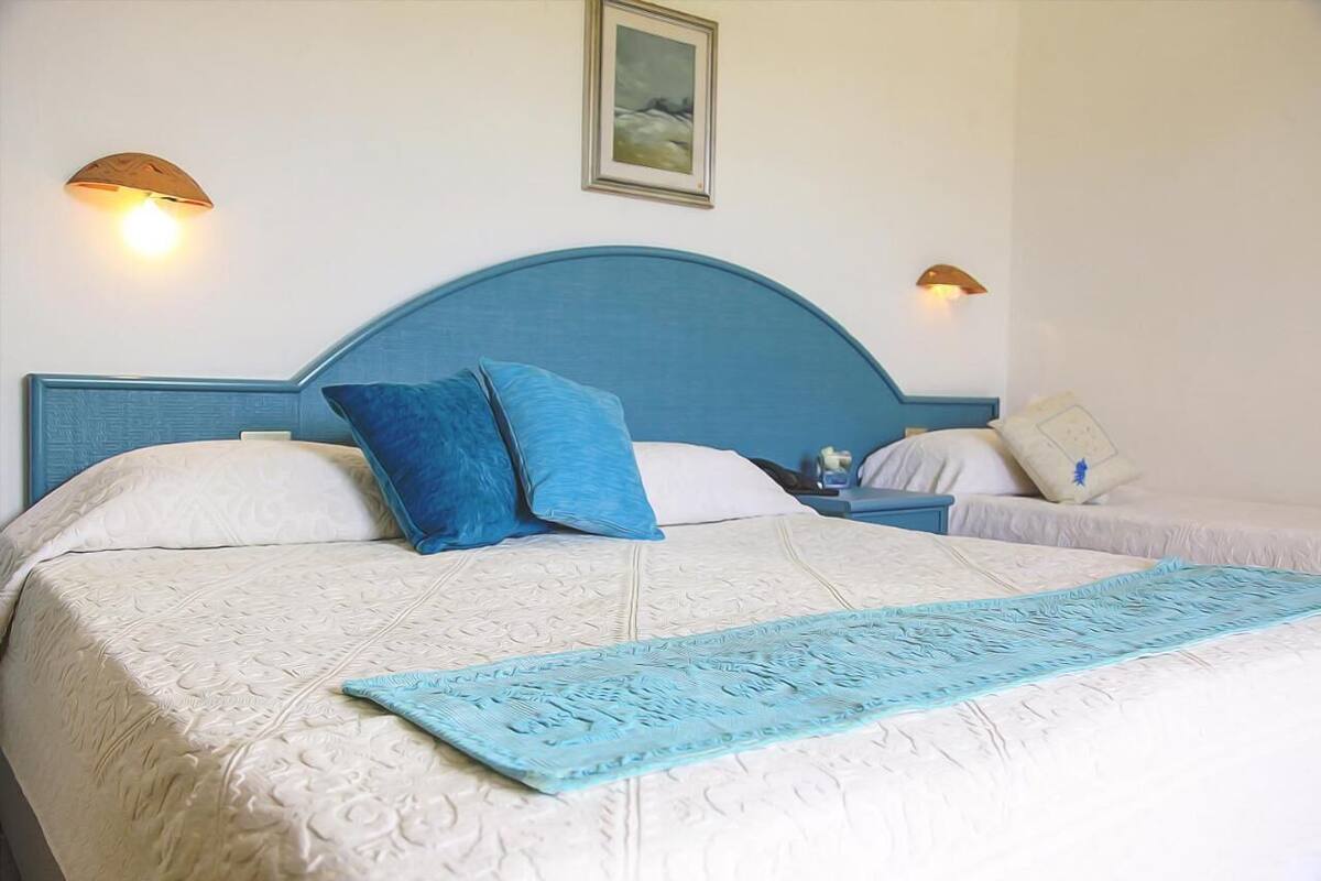 A hotel room with a large bed, two bedside tables, and wall-mounted lamps.