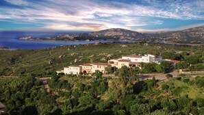 A hillside property with multiple buildings, a view of the sea, and a mountain in the background. - Hotel Micalosu (Arzachena)