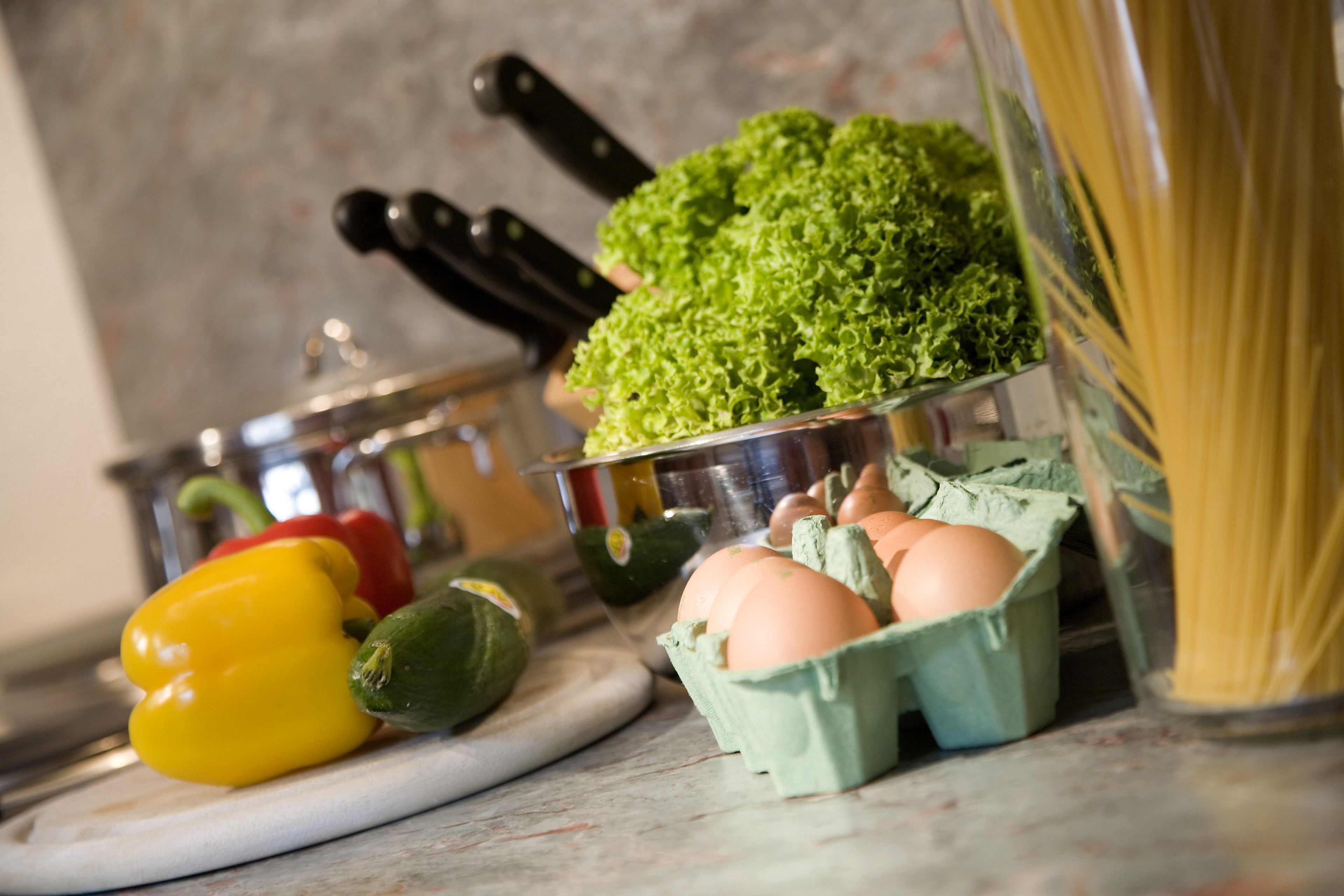 A kitchen counter with vegetables, eggs, and pasta.