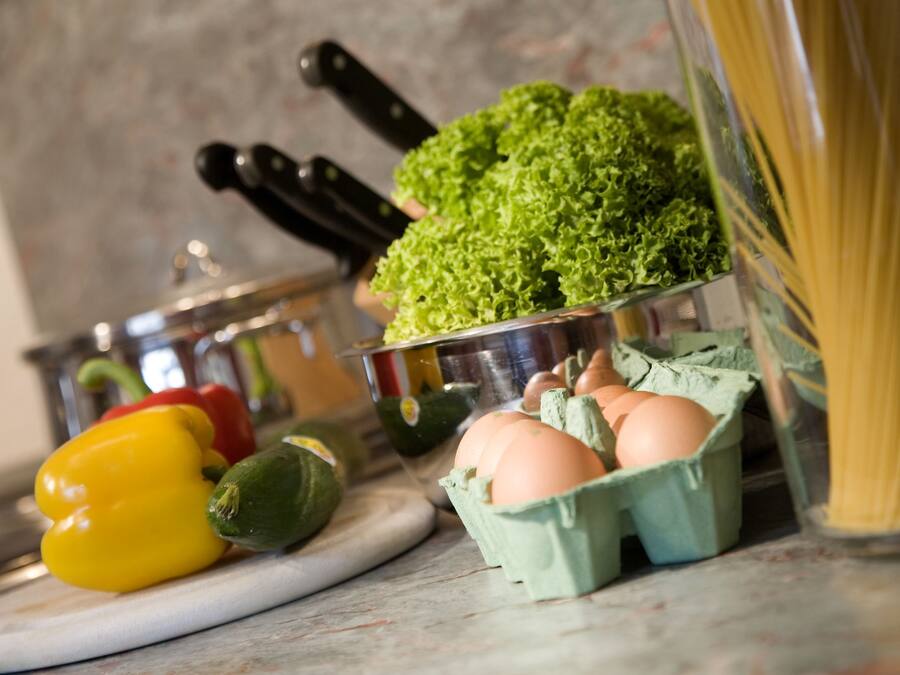 A kitchen counter with vegetables, eggs, and pasta.