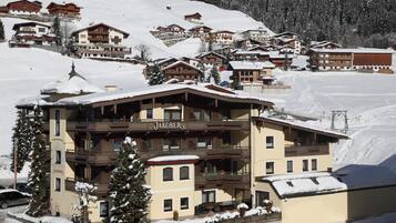 A Jakober building with a balcony, surrounded by snow-covered buildings and a ski slope in the background.