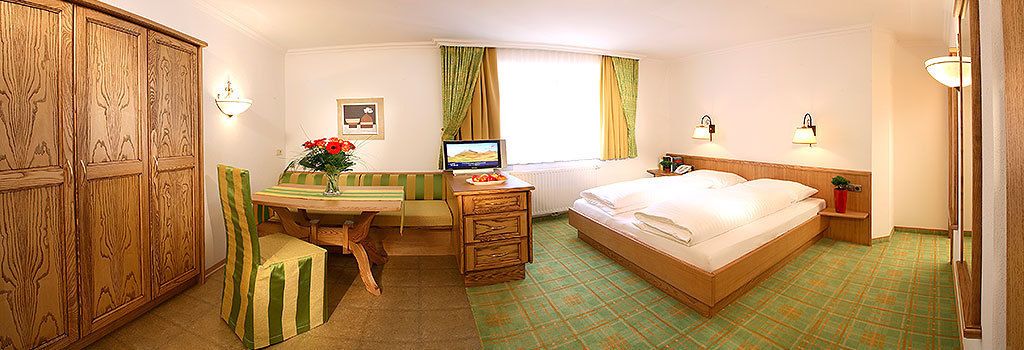 Habitación de hotel con cama, escritorio con ordenador, silla, armario y ventana con cortinas.