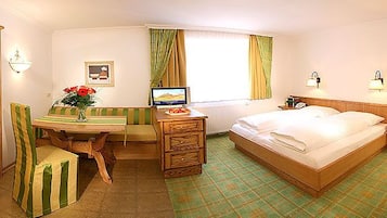 Habitación de hotel con cama, escritorio con ordenador, silla, armario y ventana con cortinas.