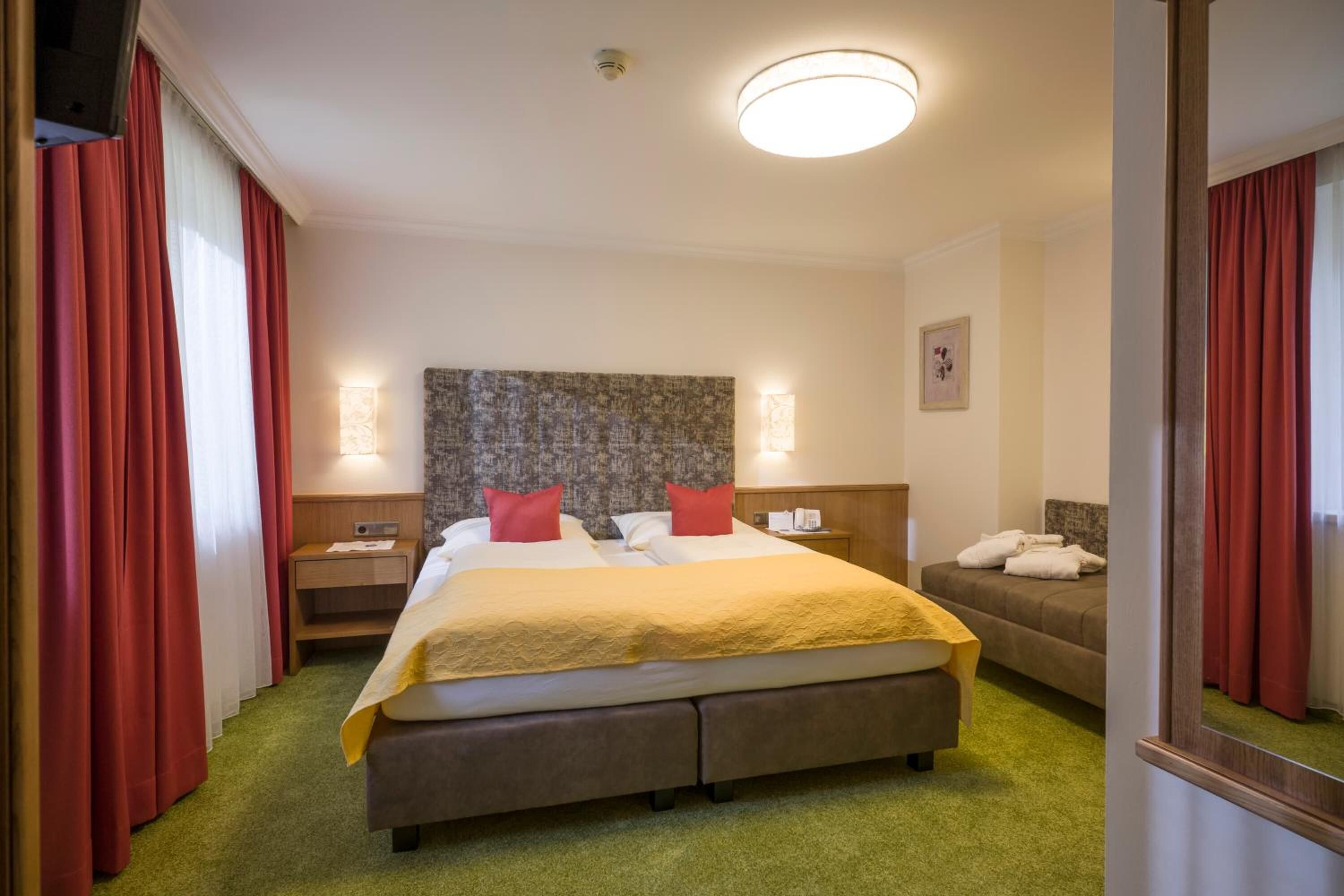 Habitación de hotel con una cama grande, cabecera con textura, dos mesitas de noche con lámparas y alfombra verde.