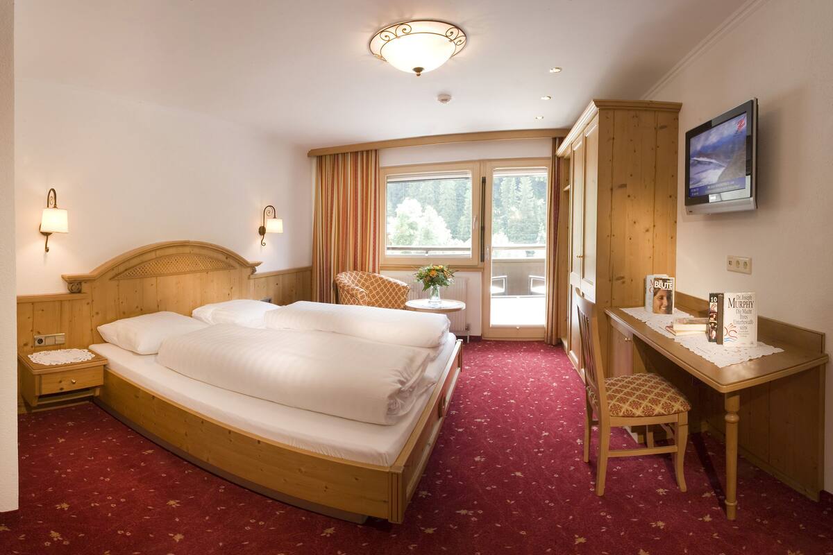Habitación de hotel con una cama grande, un escritorio, una silla, un televisor y una ventana con cortinas.