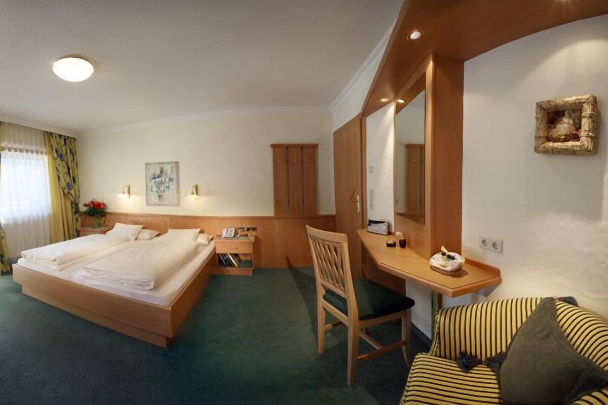 Una habitación de hotel con cama, escritorio, silla, televisor y espejo.