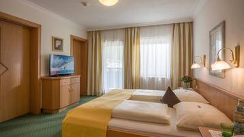 A hotel room with two beds, a television, a minibar, and a window with curtains.