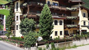 A multi-story building with a sign reading "Jakober." It features balconies with plants, a visible entrance, and a mountainous backdrop. - Hotel Jakober (Tux)