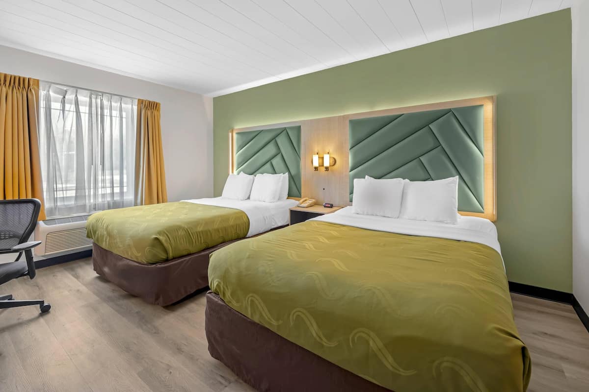 A hotel room with two beds, a desk, a chair, and a window with curtains.