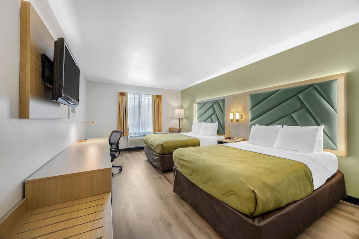 A hotel room with two beds, a desk, a TV, and a window with curtains.