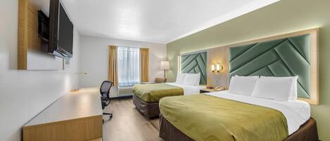 A hotel room with two beds, a desk, a TV, and a window with curtains.