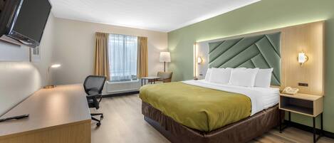 A hotel room with a bed, desk, chair, TV, lamp, and a window with curtains.