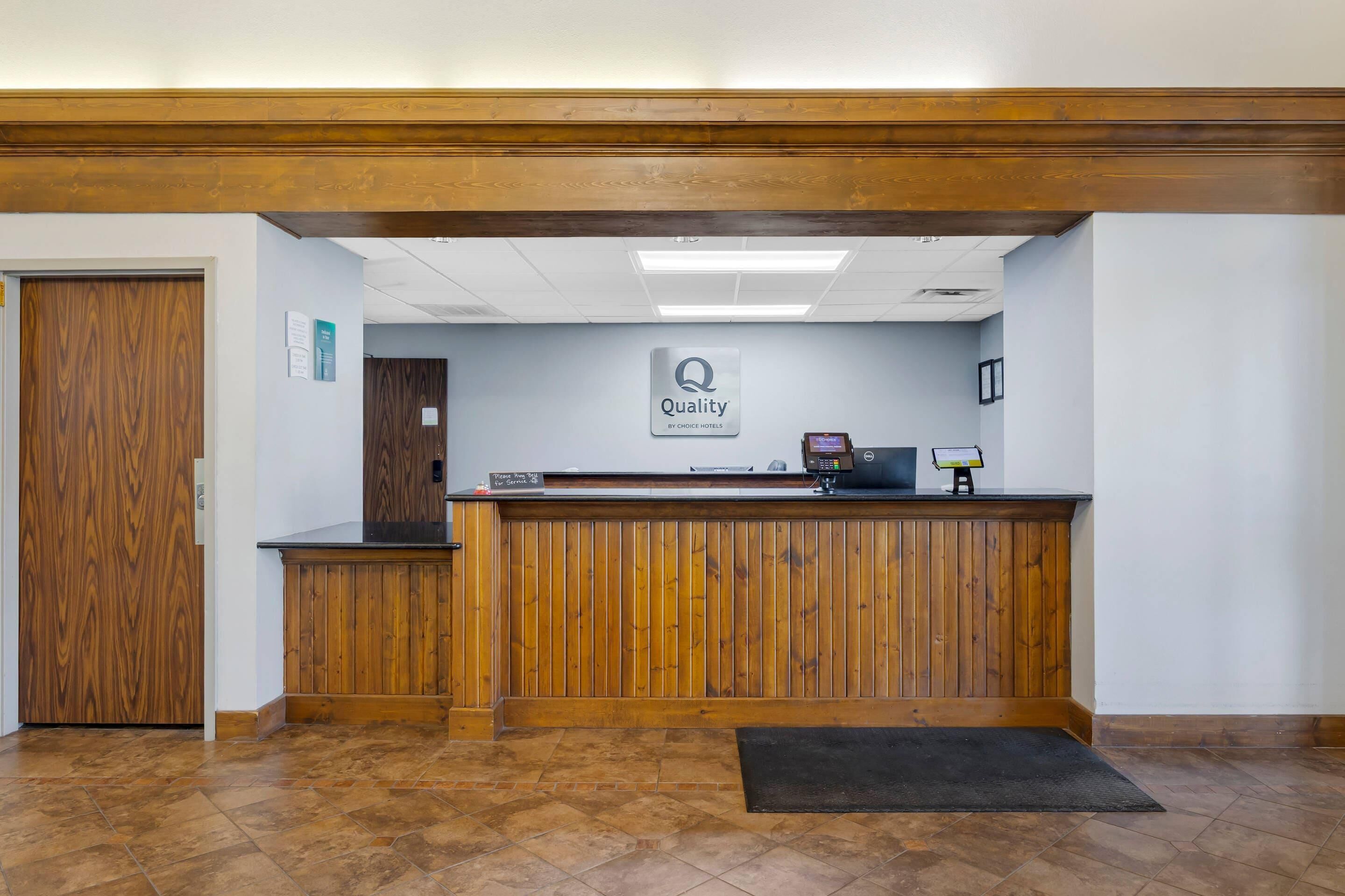 A hotel reception desk with a 'Quality by Choice Hotels' sign, a wooden reception area, and a tiled floor.