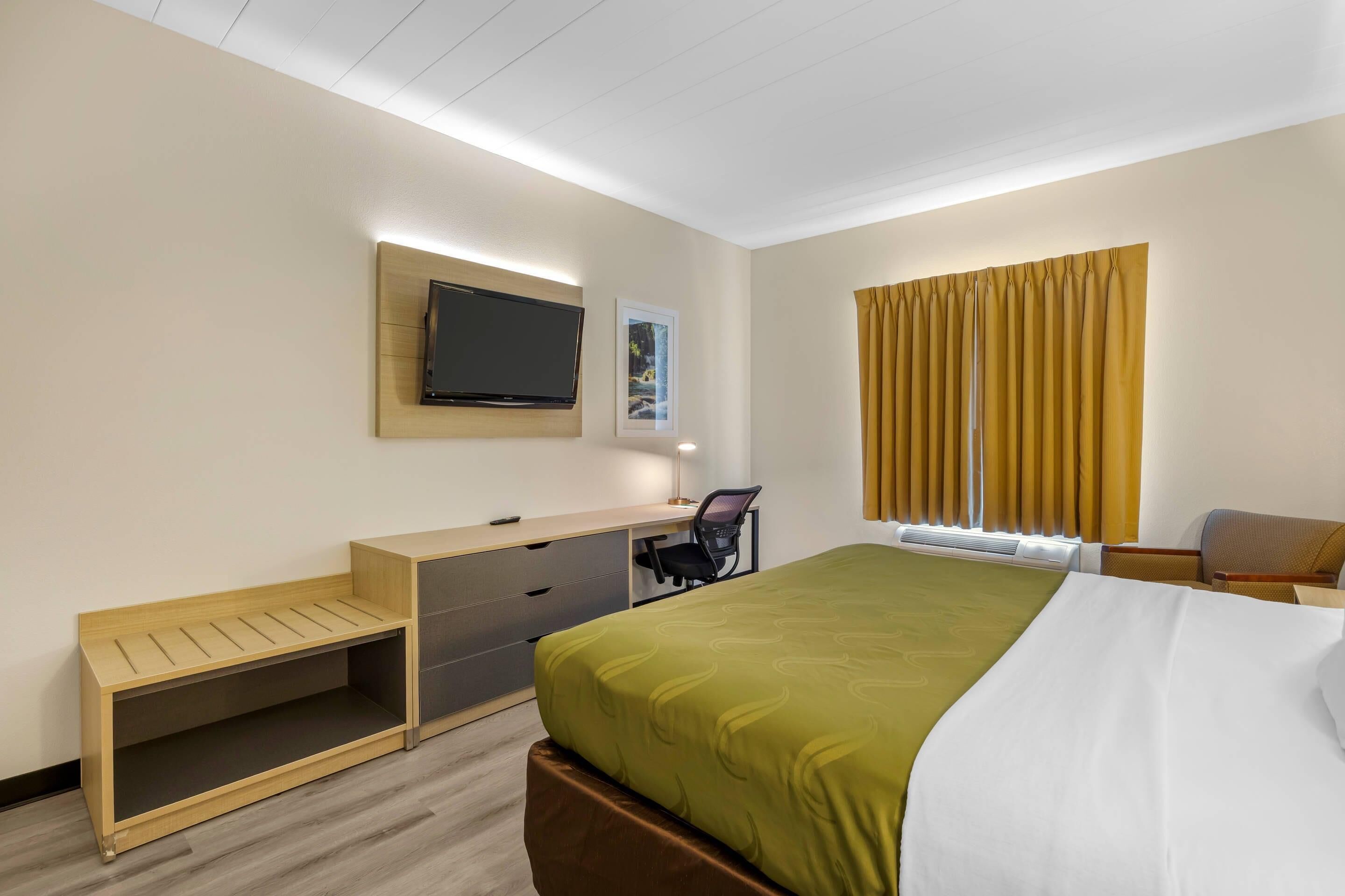 A hotel room with a bed, desk, chair, television, and a window with curtains.