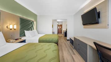 Habitación de hotel con dos camas, un escritorio, una silla, un televisor montado en la pared y piso de madera.